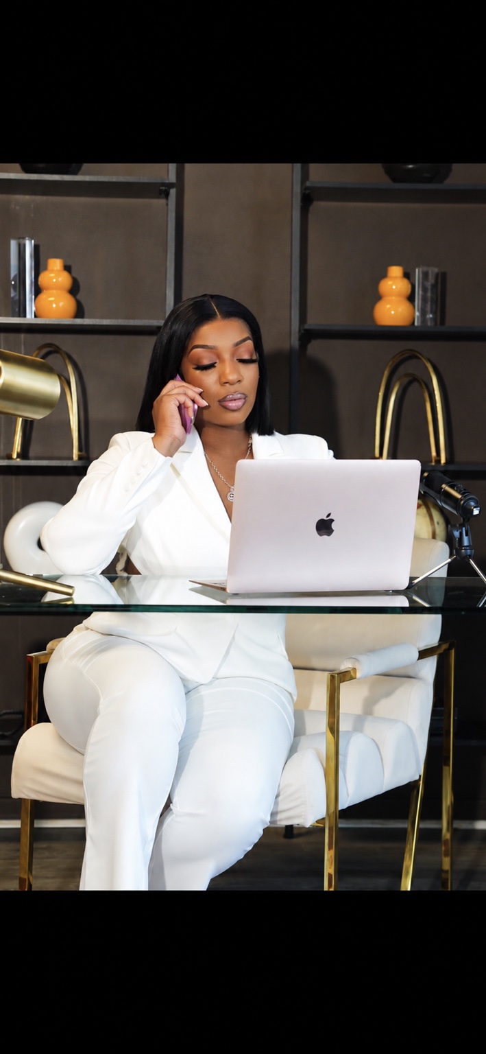 Jasmine Hodges in a white suit at her desk, speaking on the phone beside her laptop